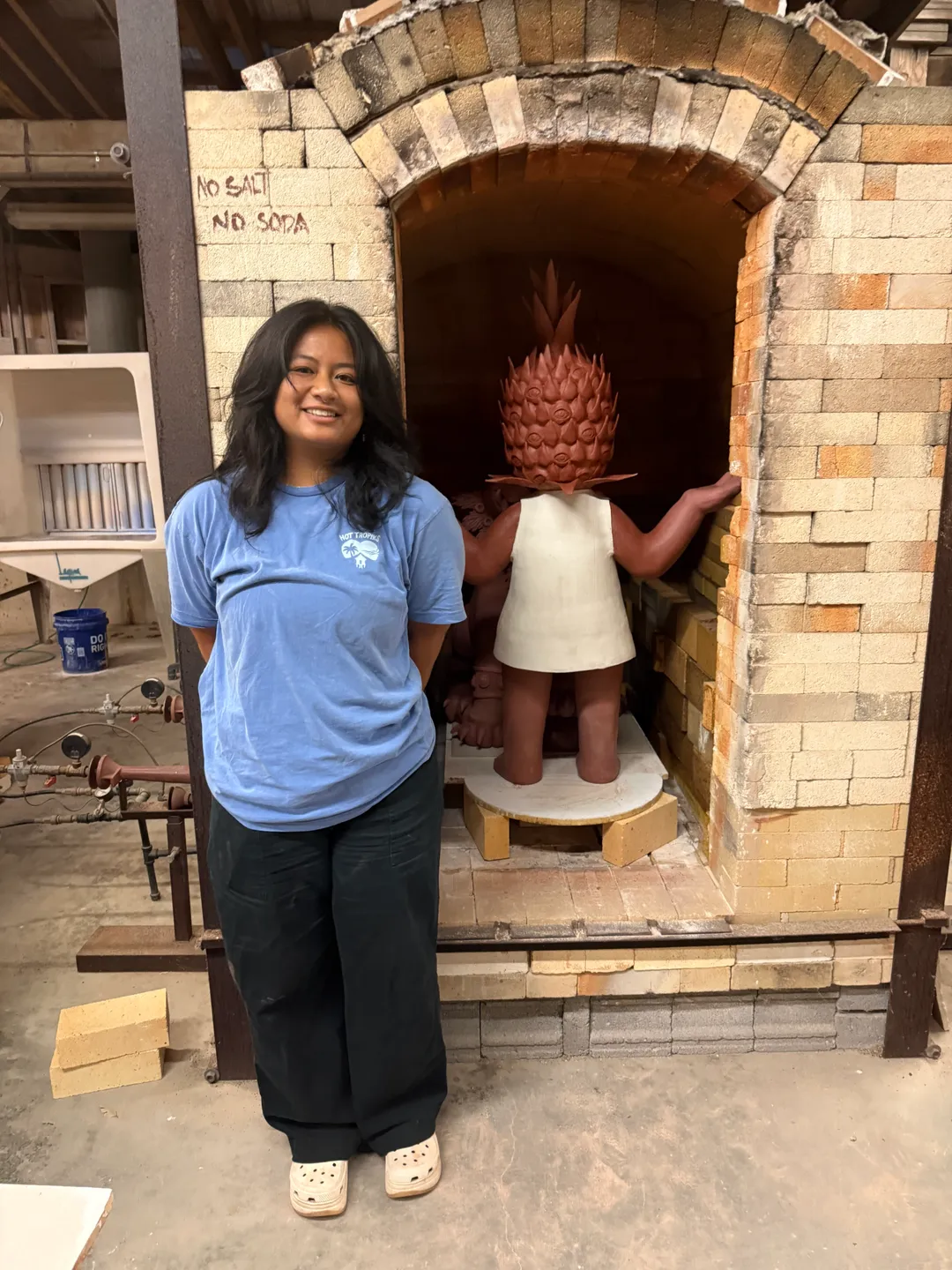 Janella next to a loaded gas kiln with her sculpture Pinya at Penland School of Craft